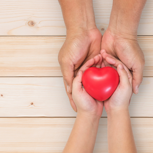 Child holding hands with adult giving a red heart